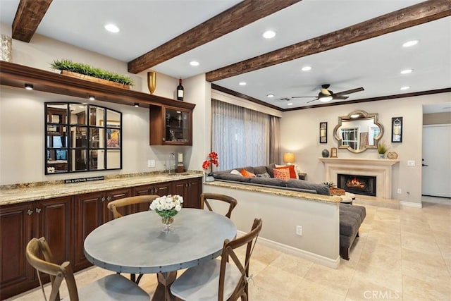 kitchen with light stone counters, open floor plan, beamed ceiling, a lit fireplace, and a sink