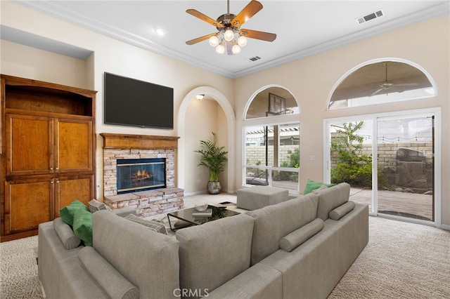 living room featuring light colored carpet, ceiling fan, a stone fireplace, and ornamental molding