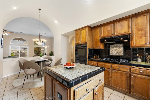 kitchen featuring a kitchen island, hanging light fixtures, black appliances, and tile counters