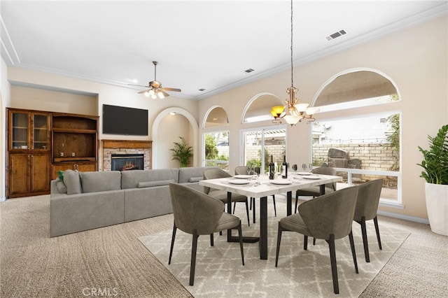 dining area featuring a fireplace, light carpet, crown molding, and ceiling fan with notable chandelier