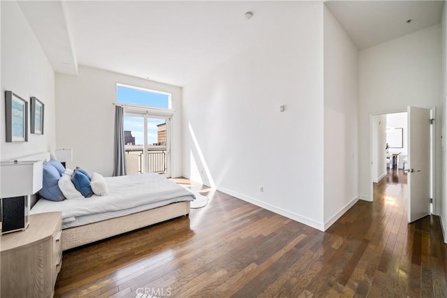 bedroom featuring baseboards, a towering ceiling, and hardwood / wood-style floors