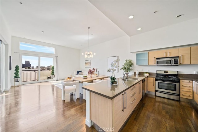 kitchen with appliances with stainless steel finishes, dark wood-style flooring, a peninsula, light brown cabinetry, and a chandelier