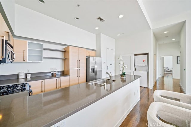kitchen featuring stainless steel appliances, a sink, visible vents, stacked washer / dryer, and open shelves