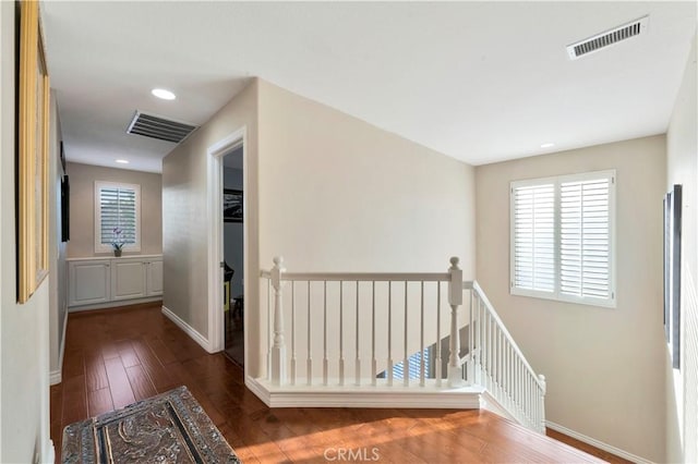 hallway with dark wood finished floors, an upstairs landing, and visible vents