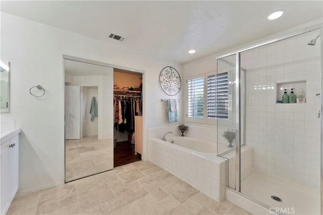 full bathroom with a walk in closet, a garden tub, visible vents, a shower stall, and vanity