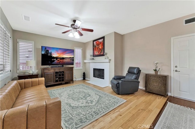 living area with baseboards, a fireplace with flush hearth, visible vents, and wood finished floors