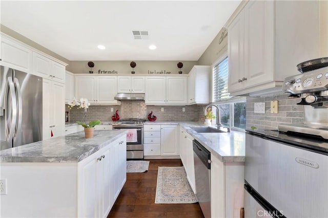 kitchen featuring a center island, stainless steel appliances, white cabinetry, a sink, and light stone countertops