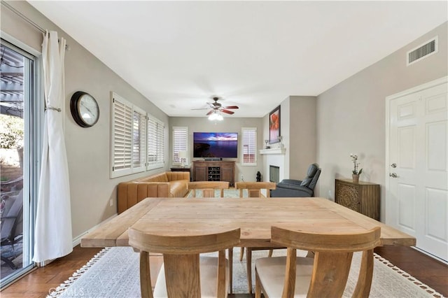 dining area featuring a fireplace, wood finished floors, visible vents, baseboards, and a ceiling fan