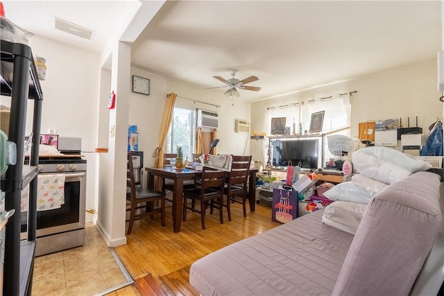 living area with light wood-type flooring, an AC wall unit, visible vents, and ceiling fan