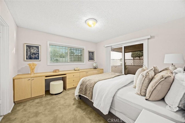 bedroom with access to outside, built in desk, a textured ceiling, and light colored carpet