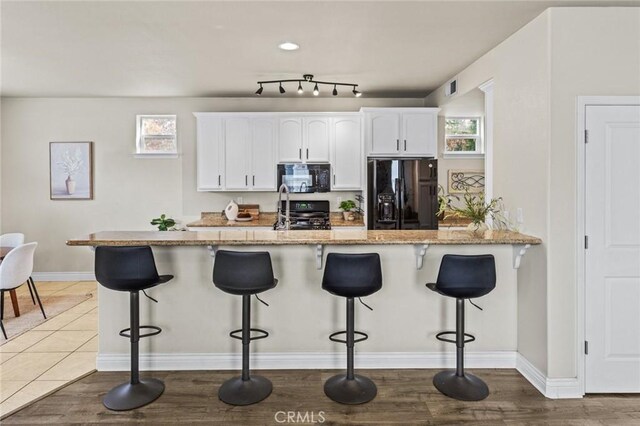 kitchen with black appliances, white cabinets, light stone counters, and baseboards