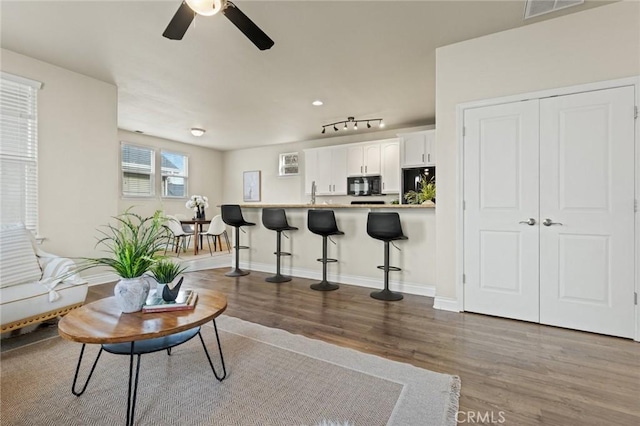 living room with ceiling fan, wood finished floors, visible vents, and baseboards