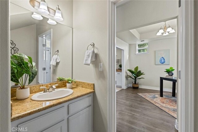 bathroom with a tray ceiling, baseboards, wood finished floors, vanity, and a notable chandelier