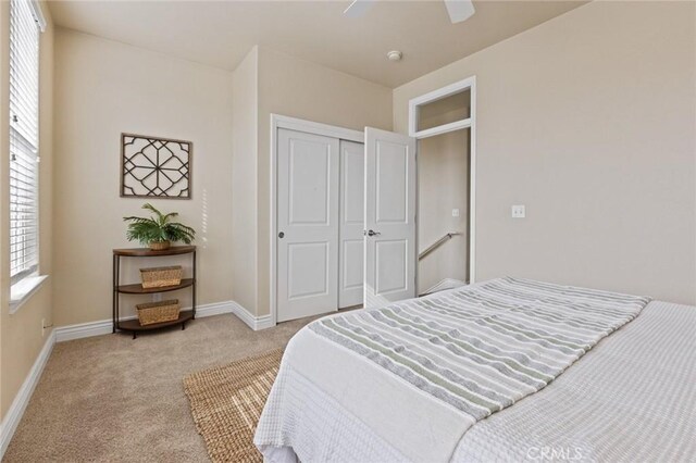 bedroom with baseboards, a ceiling fan, light carpet, and a closet
