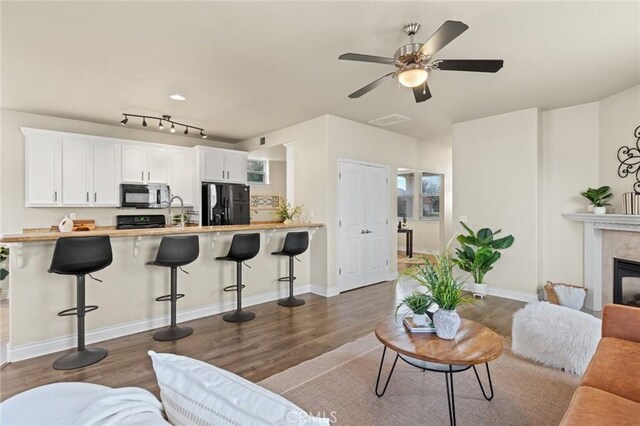 living area featuring ceiling fan, a tiled fireplace, wood finished floors, and baseboards