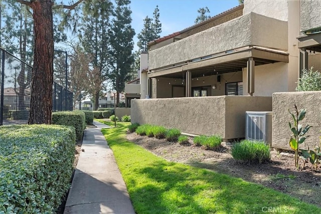 view of side of home featuring stucco siding, cooling unit, and fence