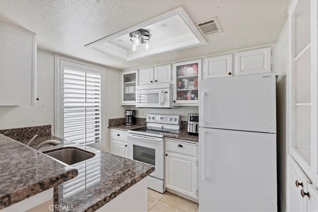 kitchen featuring white appliances, a sink, dark stone countertops, white cabinetry, and glass insert cabinets