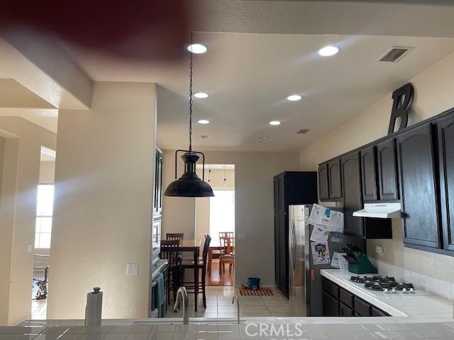 kitchen with light tile patterned floors, stainless steel appliances, dark brown cabinetry, and decorative light fixtures