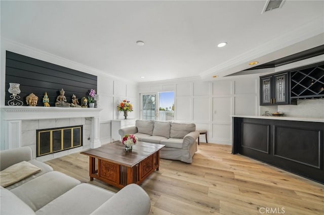 living room featuring ornamental molding, a tiled fireplace, bar, and light hardwood / wood-style flooring