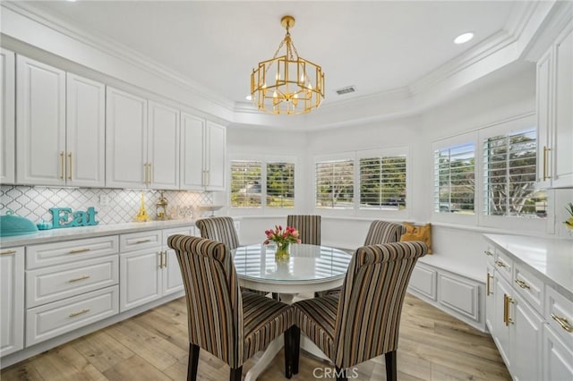 dining area with a tray ceiling, ornamental molding, an inviting chandelier, and light hardwood / wood-style flooring