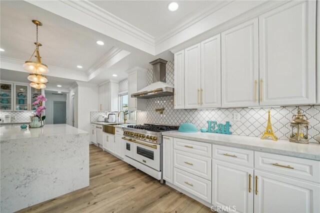 kitchen featuring double oven range, wall chimney range hood, white cabinets, and hanging light fixtures