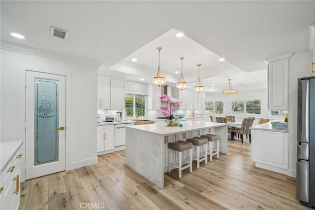 kitchen with a kitchen island, stainless steel fridge, white dishwasher, a raised ceiling, and white cabinets
