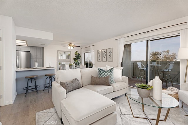 living area featuring a healthy amount of sunlight, light wood-style floors, a textured ceiling, and a ceiling fan