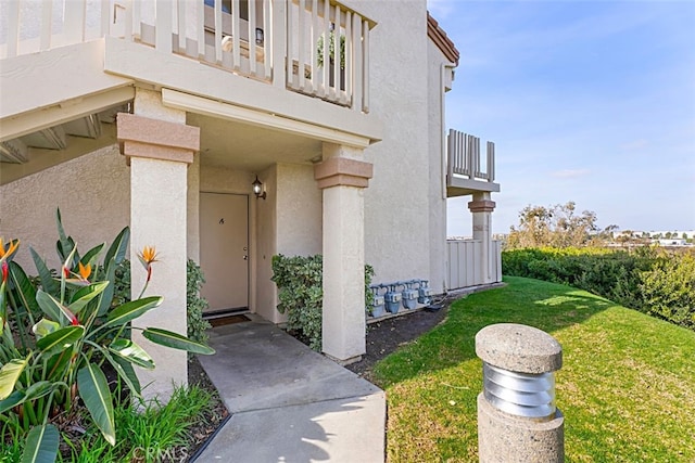 property entrance featuring a balcony, a lawn, and stucco siding