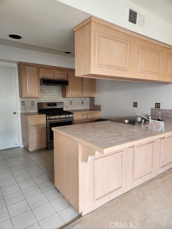 kitchen featuring tile counters, visible vents, stainless steel range with gas stovetop, a sink, and under cabinet range hood