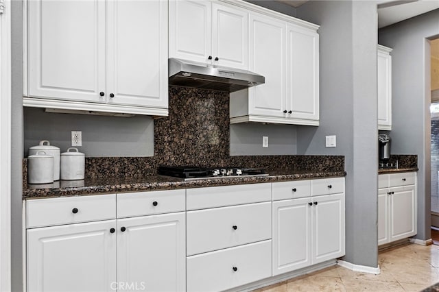 kitchen featuring gas cooktop, under cabinet range hood, white cabinetry, dark stone counters, and tasteful backsplash