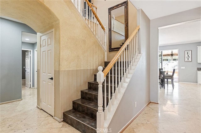 stairs featuring ceiling fan, baseboards, and arched walkways