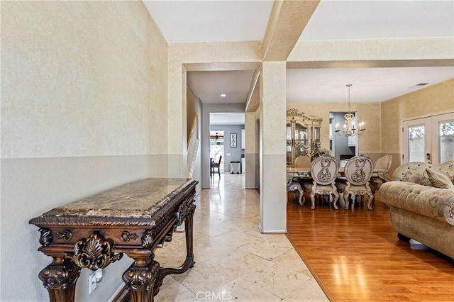 corridor with an inviting chandelier, light wood-style floors, and french doors