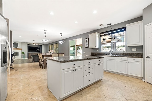 kitchen featuring a fireplace, stainless steel refrigerator with ice dispenser, visible vents, a kitchen island, and a sink