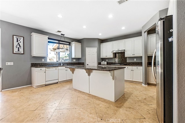 kitchen featuring a breakfast bar area, freestanding refrigerator, white dishwasher, under cabinet range hood, and white cabinetry