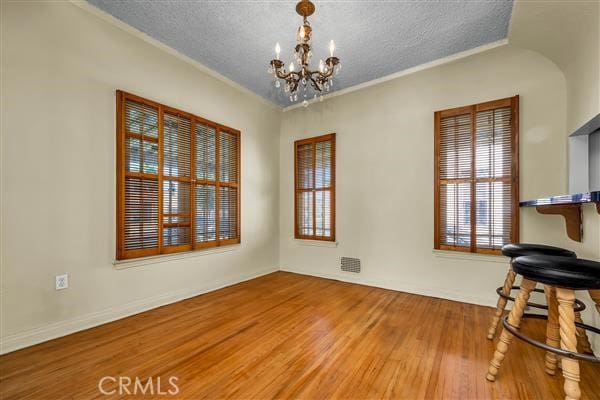 dining room with a notable chandelier, ornamental molding, wood-type flooring, and a textured ceiling