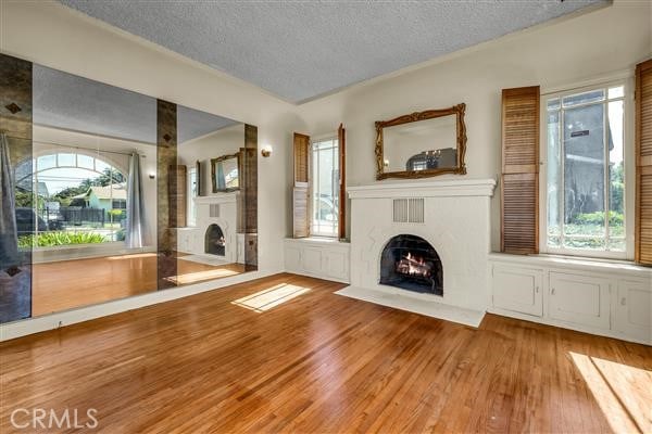 unfurnished living room featuring a healthy amount of sunlight, wood-type flooring, and a textured ceiling