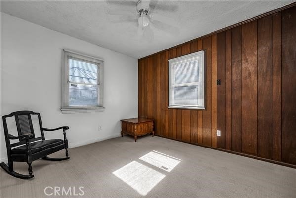 living area with ceiling fan, wooden walls, and light colored carpet