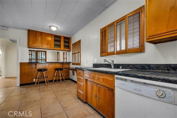 kitchen with a kitchen breakfast bar, kitchen peninsula, sink, dishwasher, and light tile patterned flooring