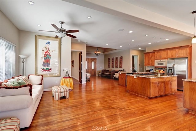 kitchen with pendant lighting, light stone countertops, wood-type flooring, appliances with stainless steel finishes, and ceiling fan with notable chandelier