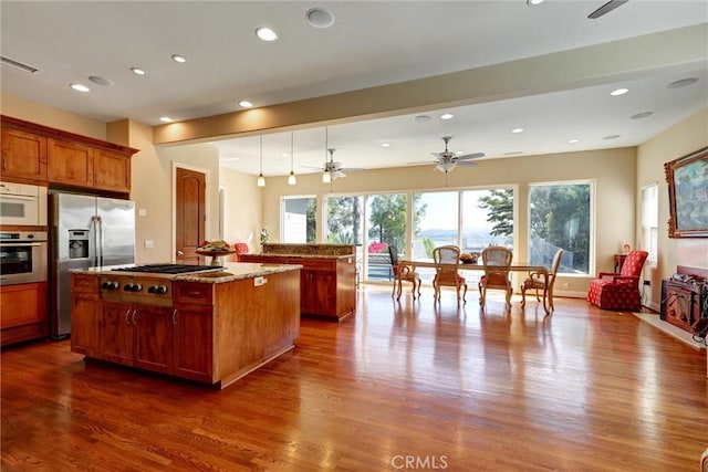 kitchen with a center island, decorative light fixtures, light stone countertops, appliances with stainless steel finishes, and dark hardwood / wood-style floors