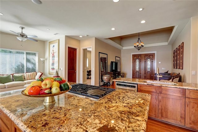 kitchen featuring stainless steel appliances, light stone countertops, sink, a tray ceiling, and pendant lighting