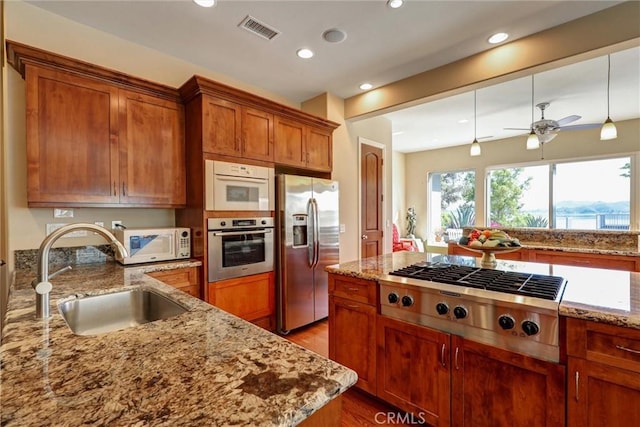 kitchen featuring sink, appliances with stainless steel finishes, light stone countertops, and pendant lighting