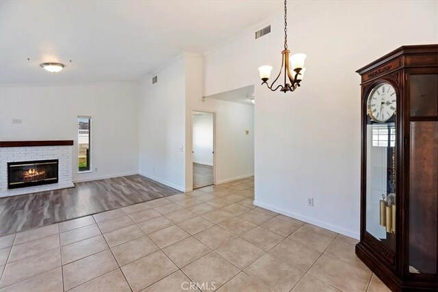 unfurnished living room featuring light tile patterned floors, a brick fireplace, visible vents, and a chandelier