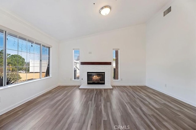 unfurnished living room featuring baseboards, visible vents, wood finished floors, crown molding, and a brick fireplace