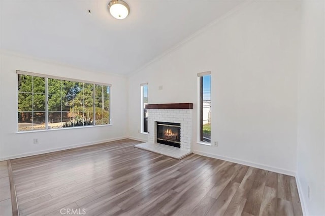 unfurnished living room with baseboards, wood finished floors, vaulted ceiling, crown molding, and a fireplace