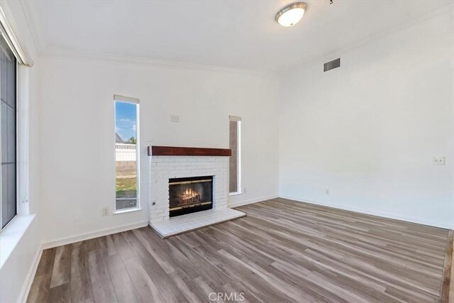 unfurnished living room with visible vents, baseboards, light wood-style flooring, ornamental molding, and a fireplace