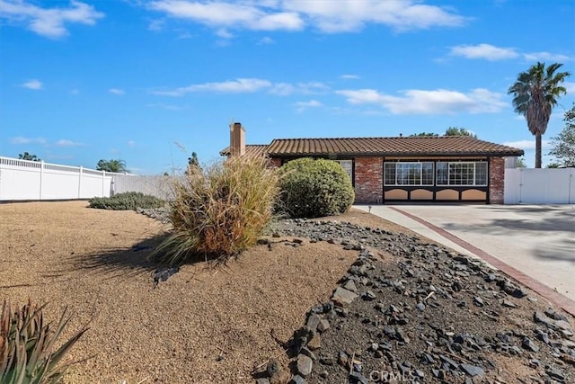 view of front of home featuring a tiled roof, brick siding, fence, and a chimney