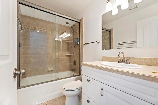 bathroom with bath / shower combo with glass door, visible vents, toilet, vanity, and tile patterned floors