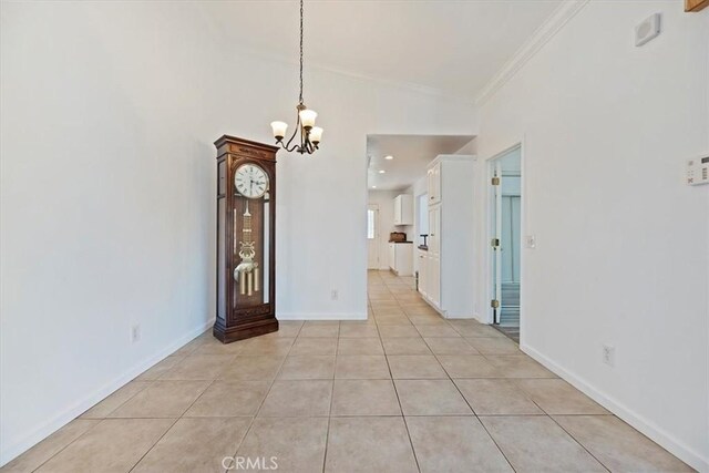 unfurnished dining area with ornamental molding, light tile patterned flooring, a notable chandelier, and baseboards