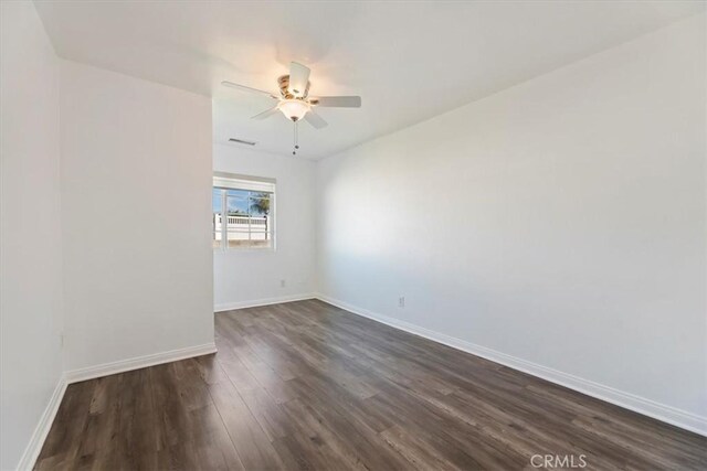 empty room featuring dark wood-type flooring, visible vents, baseboards, and a ceiling fan